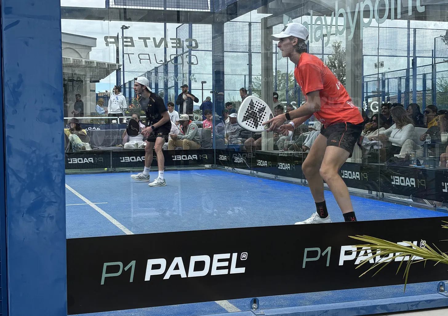 Spectators watching a padel match through the glass