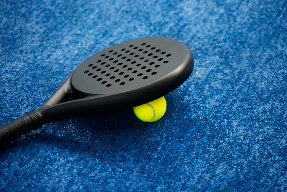 Black padel racket and ball resting on a blue court